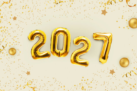 Happy New Year 2027 background with golden foil number balloons, christmas balls, glitter stars, confetti, and serpentine on light beige background. Festive holiday banner and greeting design.