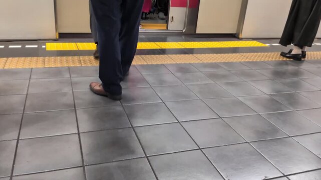 Feet of commuters boarding crowded train on station platform during rush hour in Tokyo Japan