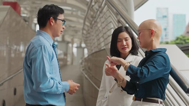 Three professionals converse on a modern urban walkway. Man in a light blue shirt listens attentively