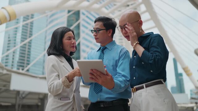 Three professionals collaborate outdoors near modern architecture. They focus on a tablet, discussing content with engaged expressions