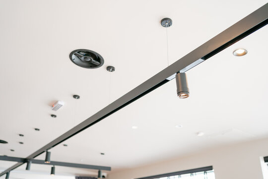 Close-up low angle view of a modern white ceiling with black track light fixtures, spot lamps, and ventilation diffusers in a contemporary commercial building