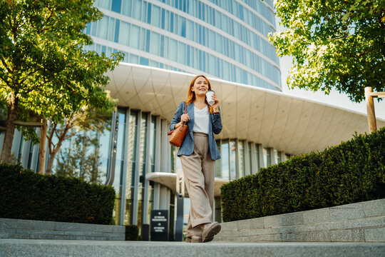 Businesswoman walking with coffee outside a modern office building