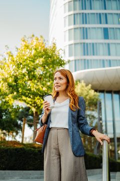 Businesswoman holding coffee outside a modern office tower