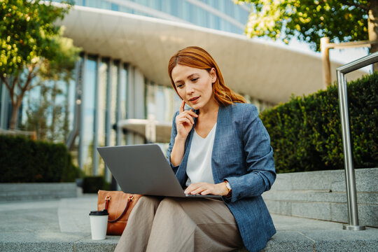 Businesswoman working on a laptop outdoors near a modern office building