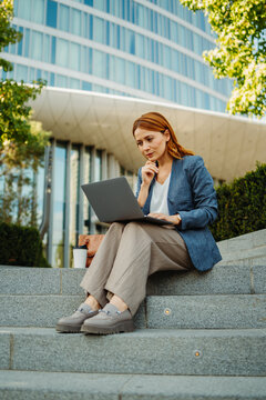 Businesswoman working remotely on a laptop outside a modern office building