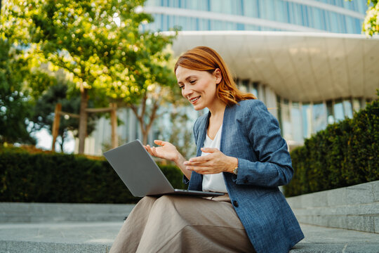 Businesswoman working remotely outdoors with laptop in an urban park
