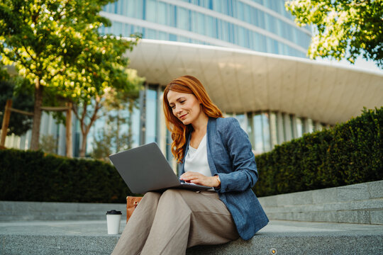 Professional woman working remotely on a laptop outside a modern office