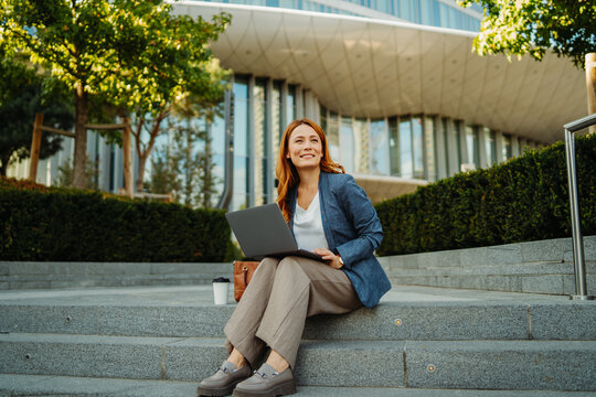 Businesswoman working remotely with a laptop outside a modern office building