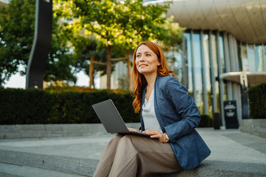 Businesswoman working remotely on a laptop outside a modern office