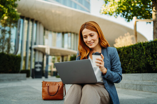 Businesswoman working on a laptop outdoors with takeaway coffee