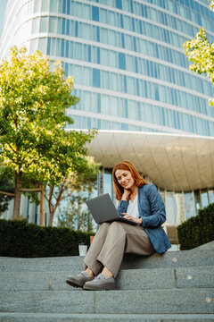 Businesswoman working on a laptop outside a modern office building