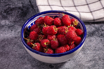 Grey stone surface with blue rimmed ceramic bowl filled with red raspberries, fresh berry fruit © Andrei Starostin