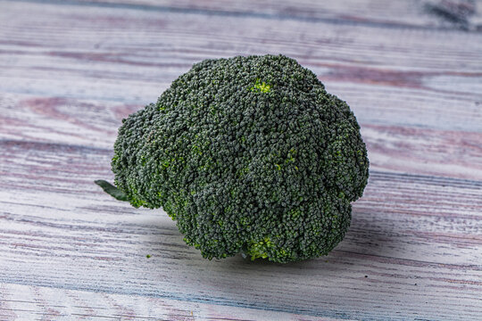 Fresh broccoli head on weathered wooden surface, vibrant green florets with natural texture, healthy vegetable ingredient