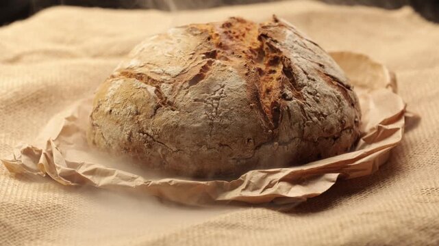 A round, rustic sourdough loaf with a crispy, crackled crust, dusted with flour and resting on crumpled brown wrapping paper in vintage style