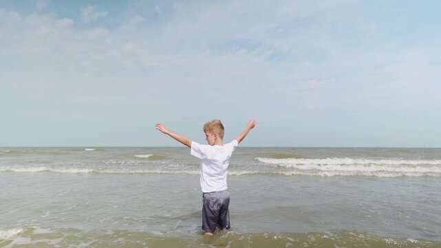 Boy standing in shallow seawater raising arms up and spinning around