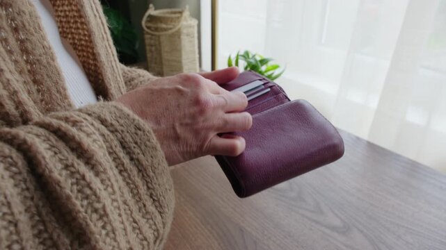 Close-up of a woman in a knitted cardigan opening her burgundy leather wallet and checking for money or credit cards inside.