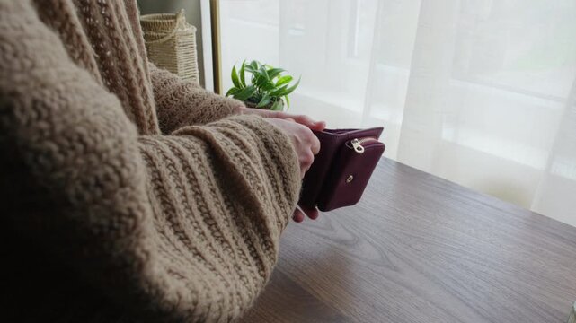 Close-up of a woman opening her wallet, taking out a stack of fifty euro banknotes, and placing the cash on a wooden table at home.