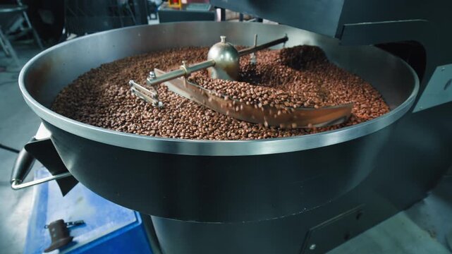 Freshly roasted coffee beans cooling turning inside automatic industrial machinery close up view of hot brown grains settling in a factory roaster after production processing drink preparation indoor