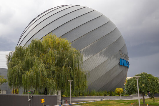 Spherical IMAX cinema building with silver metal cladding behind a weeping willow beneath an overcast sky - Bucuresti, Romania - October 16 2026