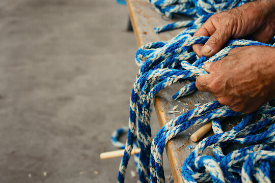 Weathered hands splicing a thick blue and white rope on a bench