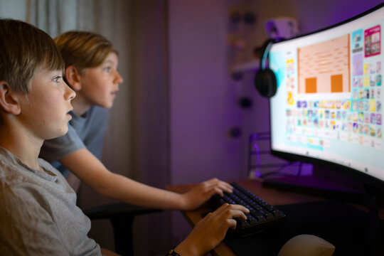 Focused boy playing games with younger brother on desktop PC in bedroom