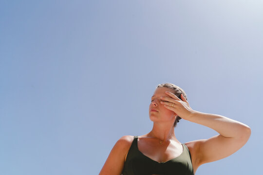 Low angle view of woman with eyes closed shielding her face from bright sunlight