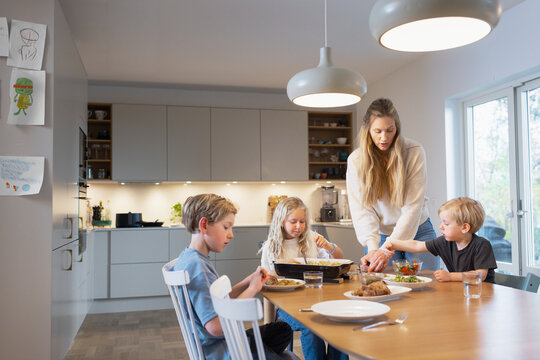 Woman serving food to her children sitting around dining table during lunch time
