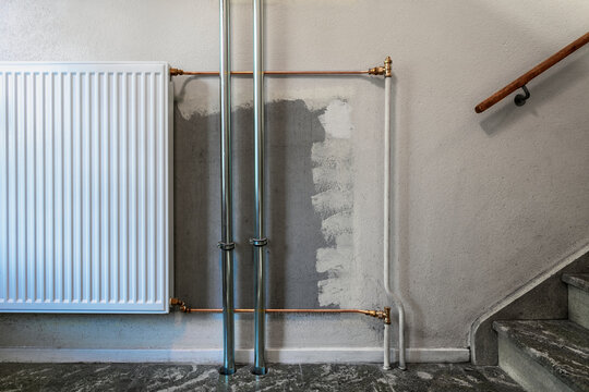 White radiator heater mounted on wall next to plumbing pipes