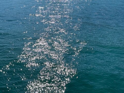Blue sea water with sun glints reflecting off the ripples on the surface. 