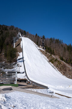 Ski flying hill Letalnica with snow-covered landing slope, judges tower and forest in winter sunlight at Planica Nordic Centre, Slovenia against blue sky