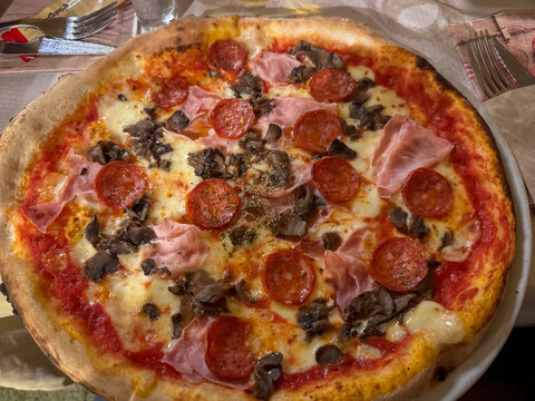 Simple and delicious freshly baked pizza with salami, ham, mushroom, melted cheese and tomato sauce served on a restaurant table