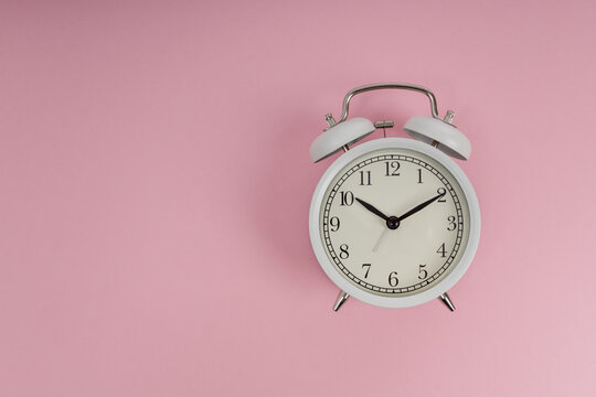 White retro alarm clock on pink background, morning routine, deadline and time management concept