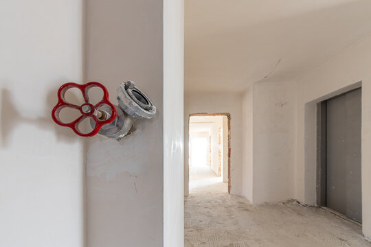 Fire hydrant valve with red handle on wall in unfinished building hallway under construction, indoor safety system and renovation concept