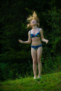 Joyful teenage girl in bikini flipping wet hair in the air outdoors on sunny summer meadow