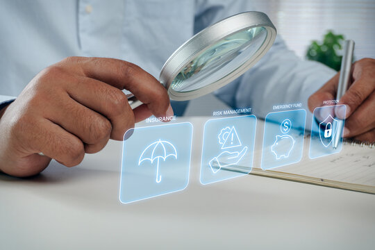 Businessman holding magnifying glass to inspect insurance and risk management digital interface overlay while writing on notebook, concept of financial protection and emergency fund planning.