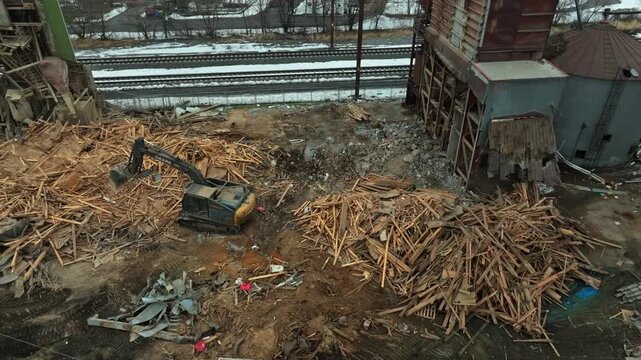 Gordonville, Pennsylvania, February 19, 2026 - An excavator works among piles of wood scraps and debris at an industrial site beside railway tracks, with snow on the ground during winter.