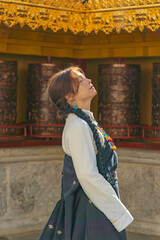 Profile of woman in Tibetan dress with head tilted back beneath a golden eave and prayer wheels, Shangri-La © nhat.photograph