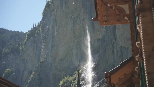 View of church in Lauterbrunnen and Staubbach waterfall in background on sunny day during summer, Lauterbrunnen, Bernese Alps, Switzerland