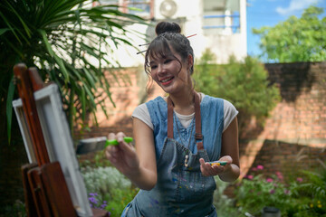 Smiling woman artist painting on canvas in a garden © Wasana
