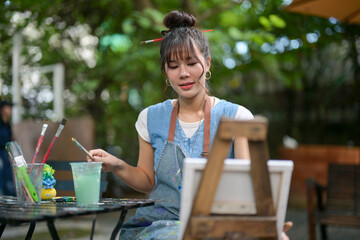 Woman painting outdoors at an easel during a focused creative session © Wasana