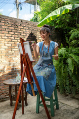 Asian woman artist painting outdoors in a garden courtyard © Wasana