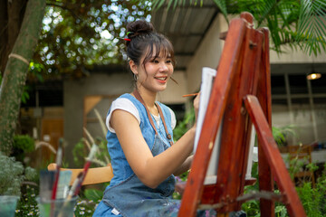 Young woman painting on an easel in a leafy outdoor art studio © Wasana