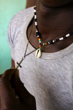 Close-up of a beaded necklace with cowrie shell and a cross on a grey shirt, Hauts-Bassins Region, Bobo Dioulasso, Burkina Faso
