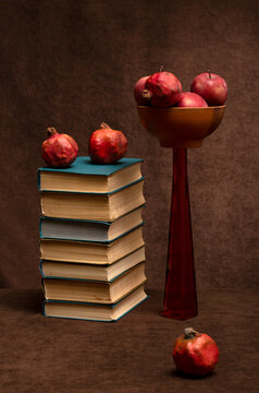 Still life with books, apples, and pomegranates on a table