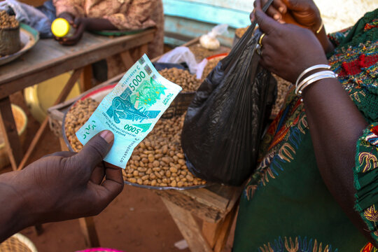Hand holding a 5000 franc CFA banknote at a peanut market stall, Cascades Region, Banfora, Burkina Faso