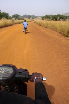 View from a motorbike on a red dirt road in Lobi tribe country with another rider ahead, Sud-Ouest Region, Gaoua, Burkina Faso
