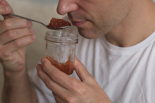 Man holding a spoon and a glass jar of red caviar