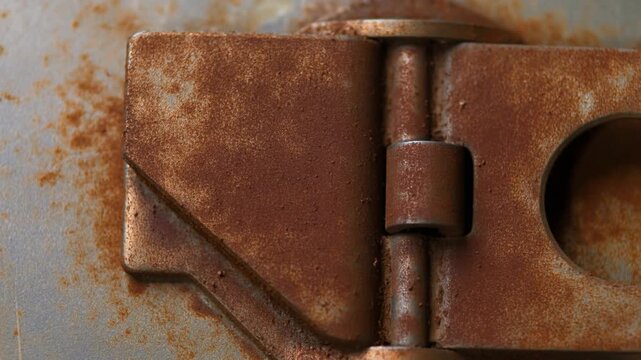 Rusty metal hinge with orange corrosion on gray steel plate, closeup static view