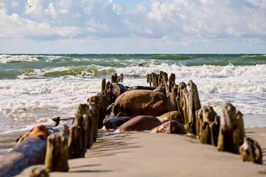 Weathered wooden breakwater extends toward rolling ocean waves under blue skies