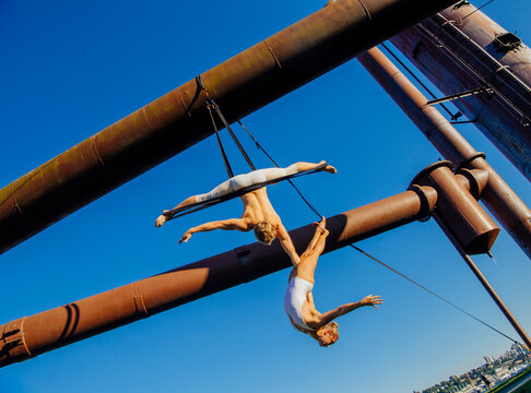 Two acrobats performing aerial straps routine outdoors with industrial